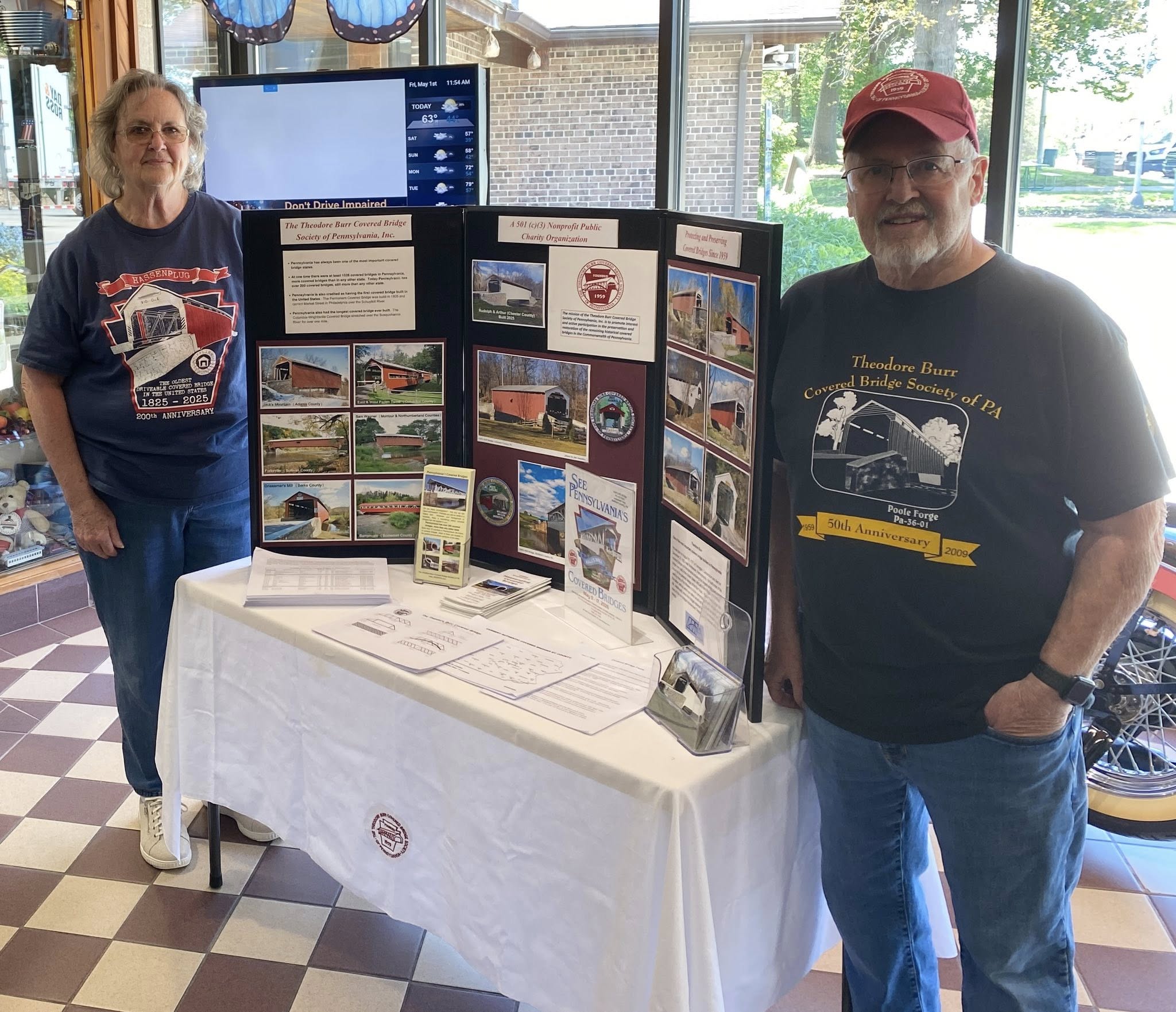 Gloria and Jim Smedley with covered bridge display at a Welcome Center
